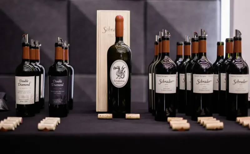 Display of Schmelzer luxury red wines in bottles and wooden box, with corks on black tablecloth
