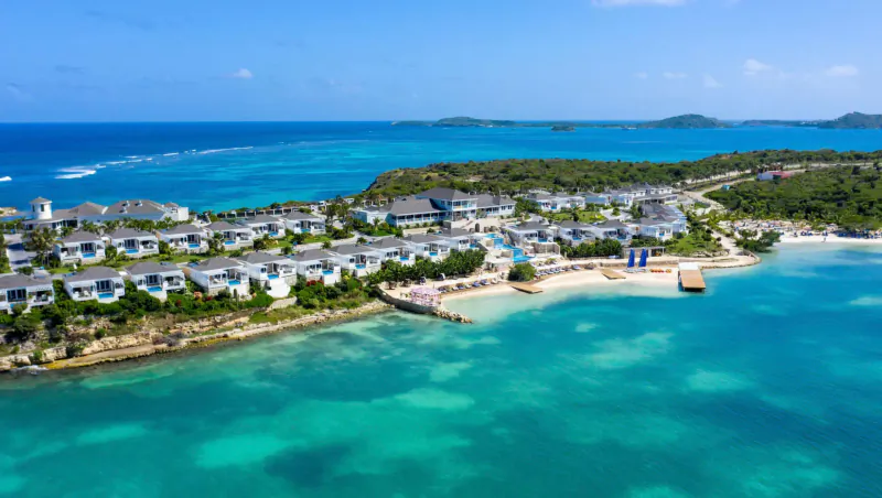 Aerial view of Hammock Cove luxury resort in Antigua, with white villas, beach, dock, and turquoise Caribbean sea.