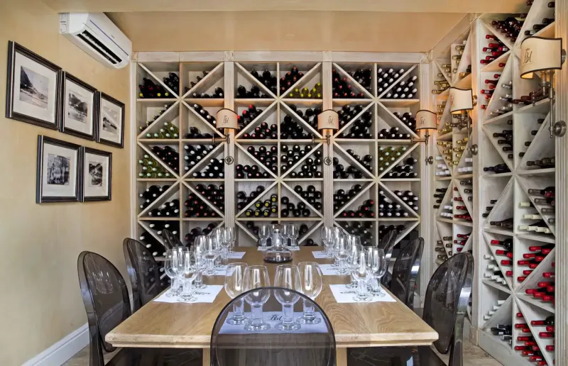 Elegant wine cellar with wooden racks full of bottles, set table with wine glasses, and framed photos on walls.