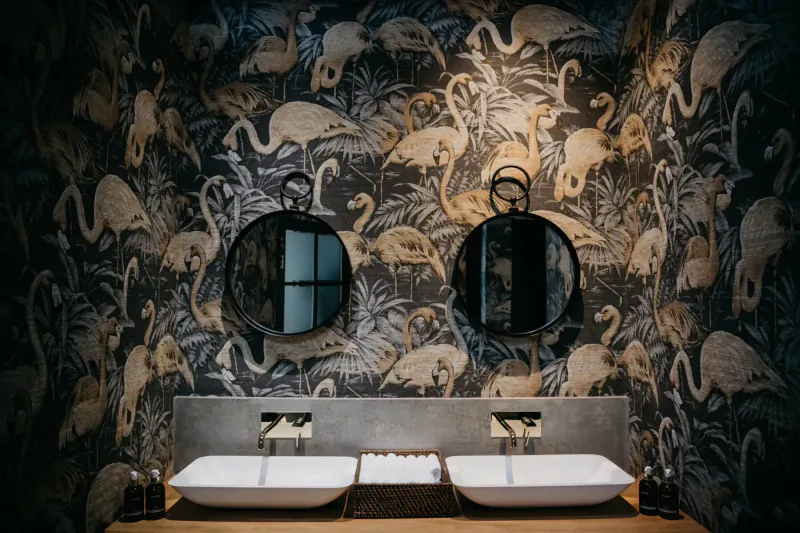 Luxurious bathroom vanity with two white sinks, black-framed round mirrors, and flamboyant flamingo wallpaper at The Old Rectory.