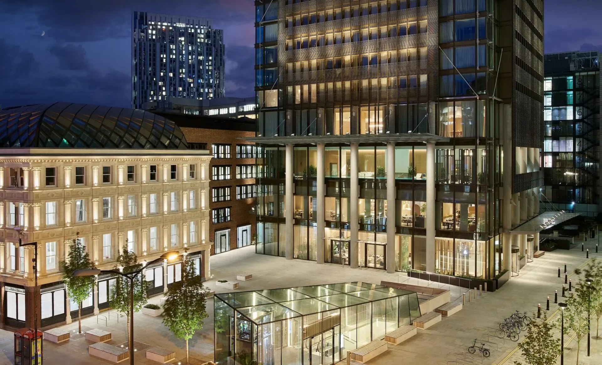 Pan Pacific London luxury hotel at dusk, modern glass tower with columns, plaza, trees, and city high-rises
