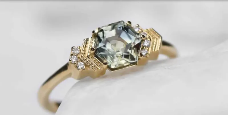 Close-up of gold hexagonal green gemstone ring with diamond accents on white surface