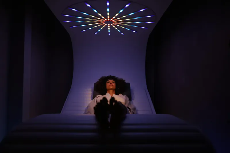 Person reclining on bed in Grey Wolfe London wellness space, gazing at vibrant radial light projection on curved ceiling.