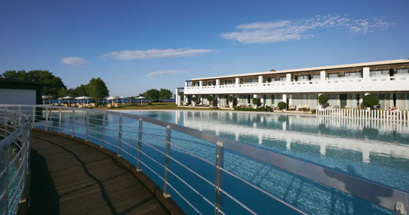 Luxury white hotel building beside large infinity pool with lounge chairs, sunny seaside view in Crete