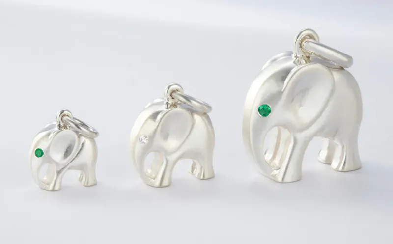 Three silver elephant charms in graduating sizes, each with a green gem eye, on chains