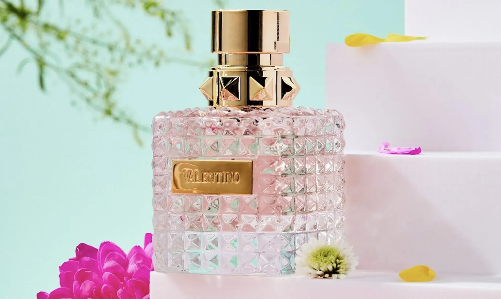 Valentino Donna Born in Roma perfume bottle with pink crystal facets and gold studded cap on steps with flowers