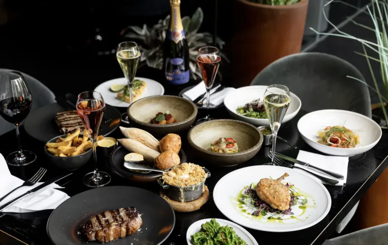 Elegant Gaucho restaurant table with steak, roast chicken, fries, salads, bread, champagne, and wine glasses.