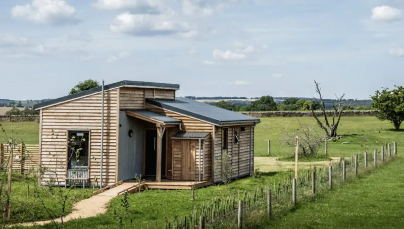 Modern wooden luxury lodge with deck in grassy Cotswold farm field under partly cloudy sky