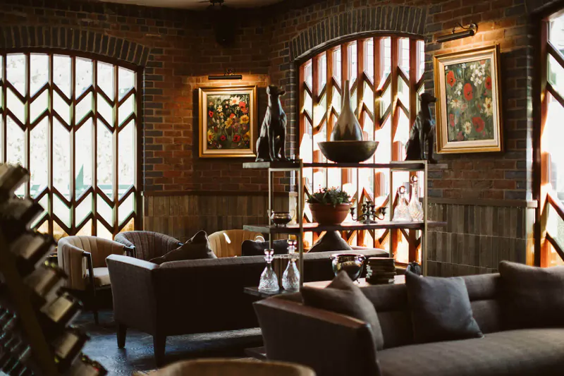 Cozy lounge in The Rabbit Hotel with brick walls, arched windows, leather sofas, plants, and art.