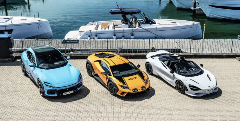 Blue Polestar 1, yellow Lamborghini Huracan STO, white McLaren 720S parked by marina dock with yachts.