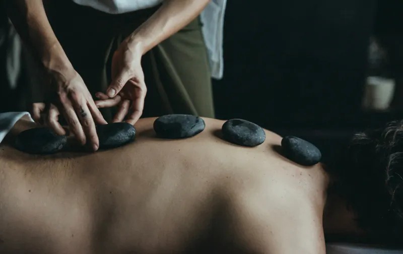 Therapist placing hot stones on client's bare back during spa treatment at Pharomatiq Spa