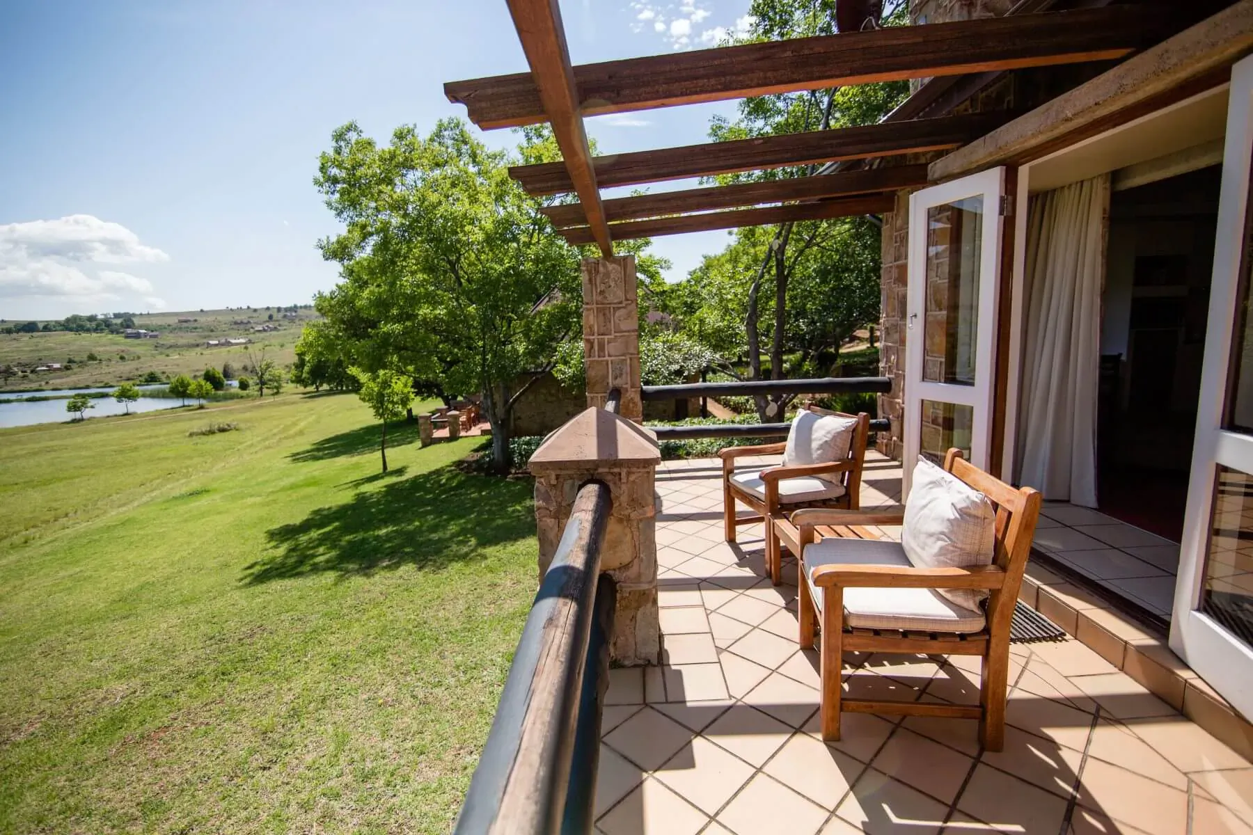 Wooden chairs with cushions on a covered stone balcony overlooking green lawns, trees, and a distant lake at Walkersons Hotel & Spa.