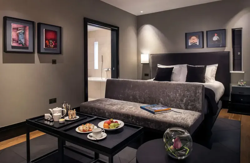 Elegant hotel room in Twr y Felin art hotel with king bed, velvet chaise, tea service, fruit plate, and abstract wall art.