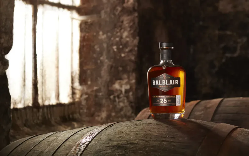 Balblair 25 whisky bottle on barrel in rustic distillery with window light
