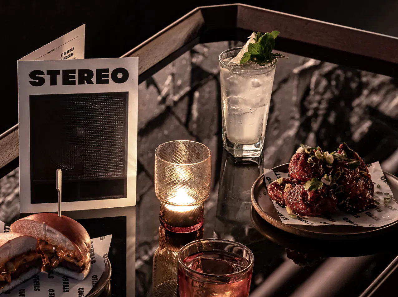 STEREOO sign, gin with mint, lit glass, chicken wings, burger on glossy table at Stereo venue