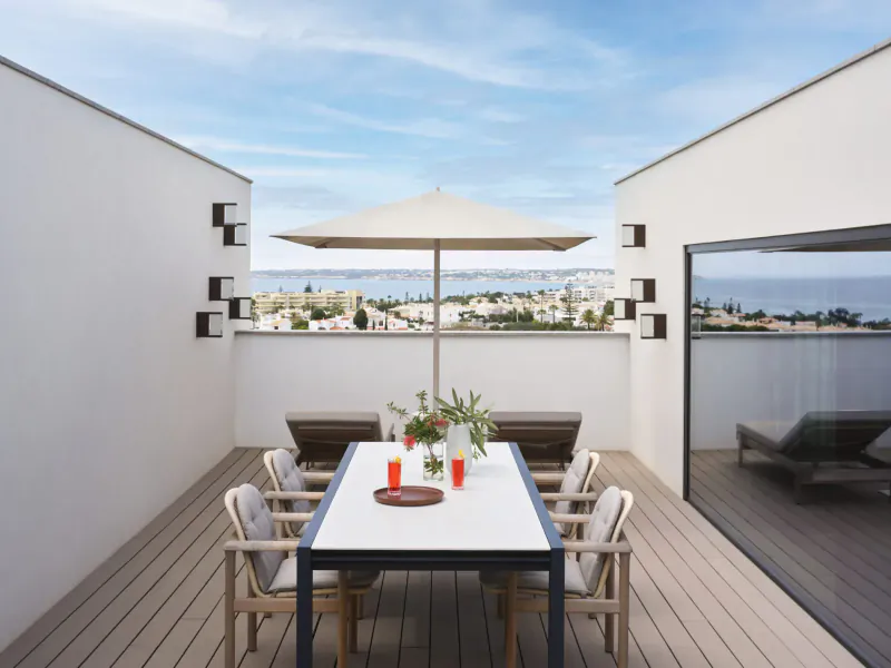 Spacious rooftop terrace at W Algarve Hotel with white dining table, chairs, umbrella, and ocean views.