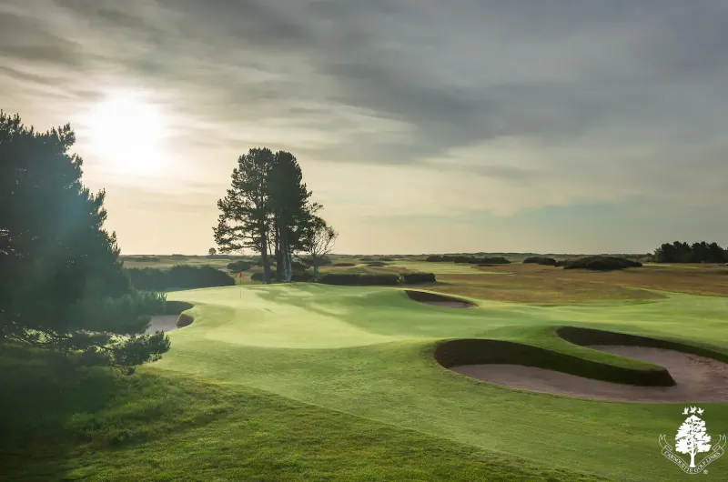 Carnoustie golf course in Scotland at sunset, green fairways, bunkers, pine trees under cloudy sky