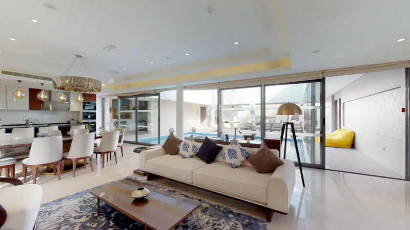Luxurious modern living room with white sofa, glass dining table, pool view through sliding doors in desert resort villa