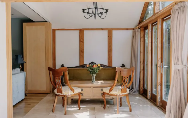 Elegant dining area in Cotswolds country house with wooden chairs, flower-adorned table, chandelier, and garden-view windows.
