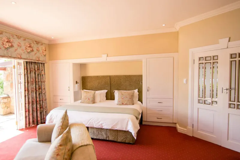 Elegant hotel bedroom with king bed, floral curtains, open doors to patio, and plush armchair.