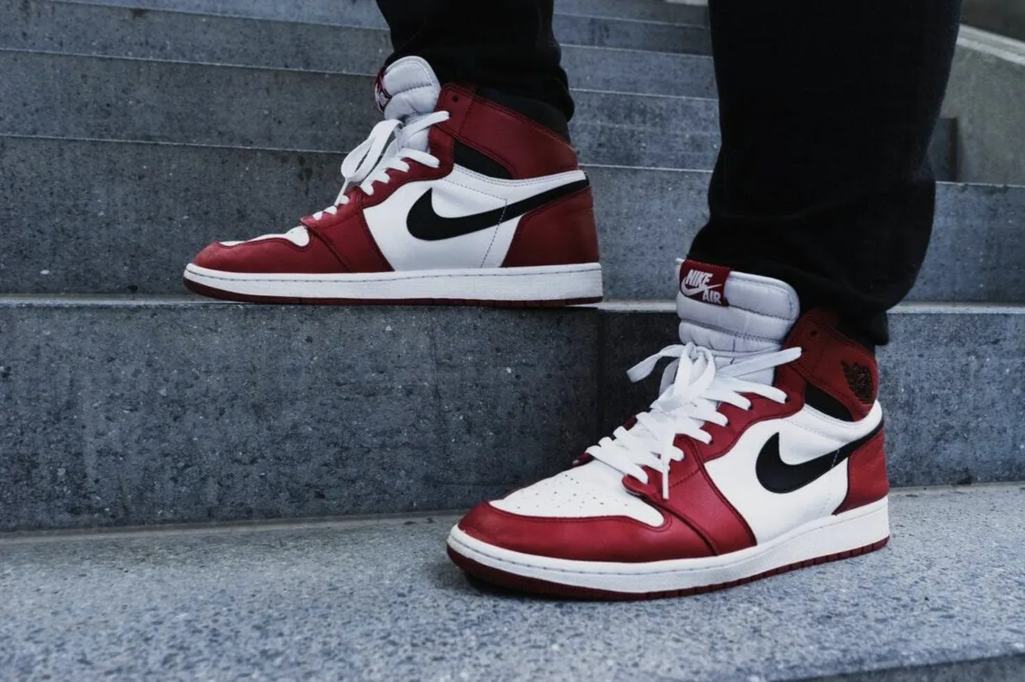 Close-up of red and white Air Jordan 1 high-top sneakers on black pants ascending concrete stairs