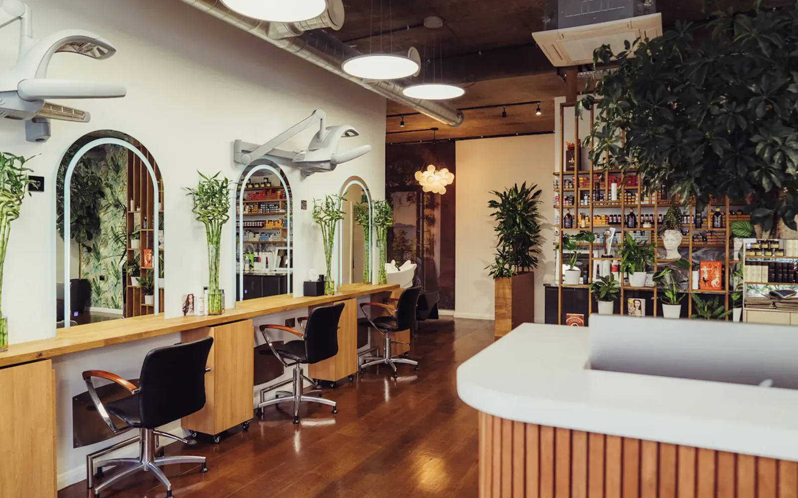 Modern Adem Salon interior in Belgravia, London: oak reception desk, black stylist chairs, mirrors, plants, and warm lighting.