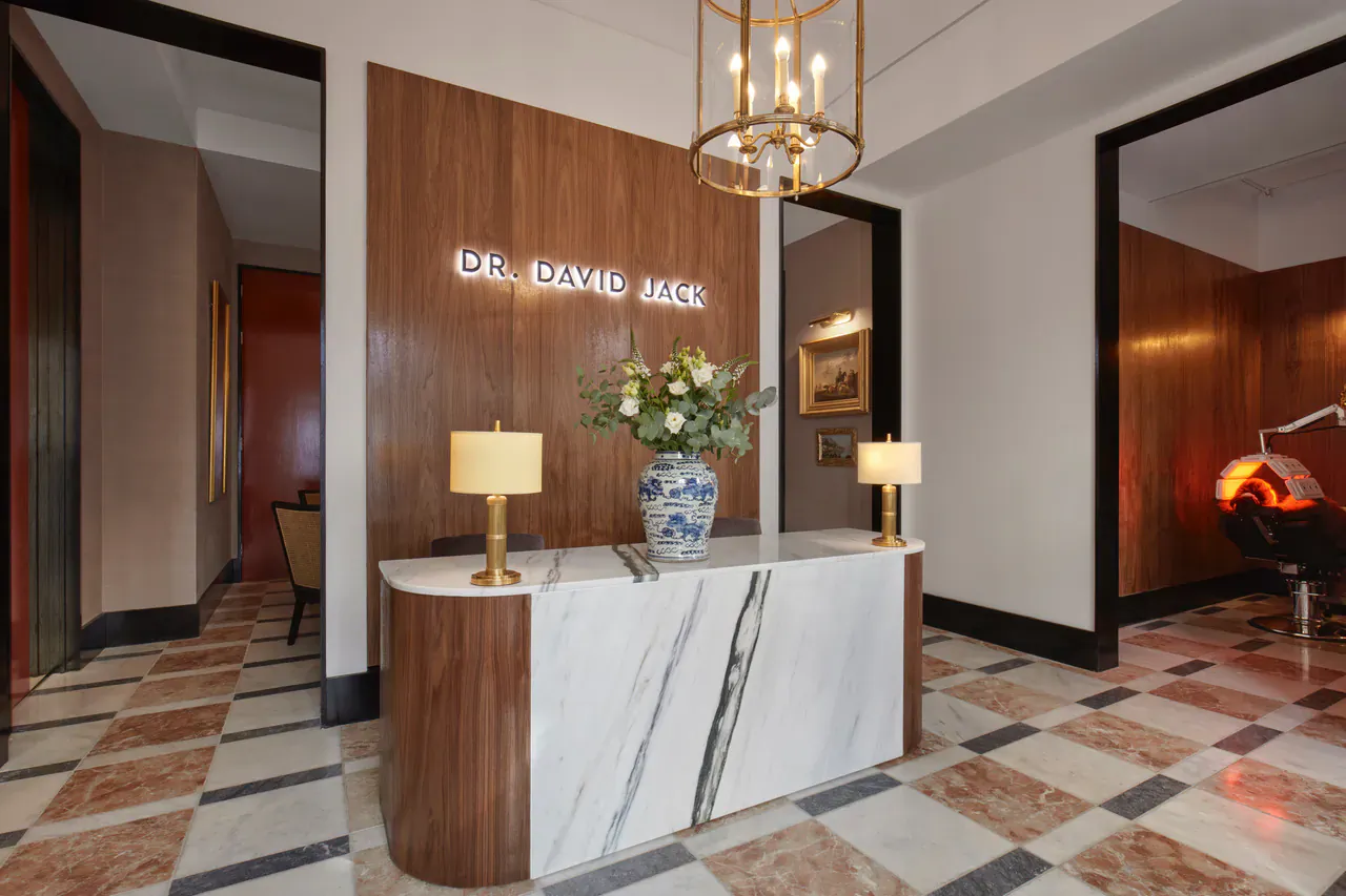 Dr David Jack London reception desk with neon sign, marble counter, blue vase of flowers, lamps, and elegant decor.