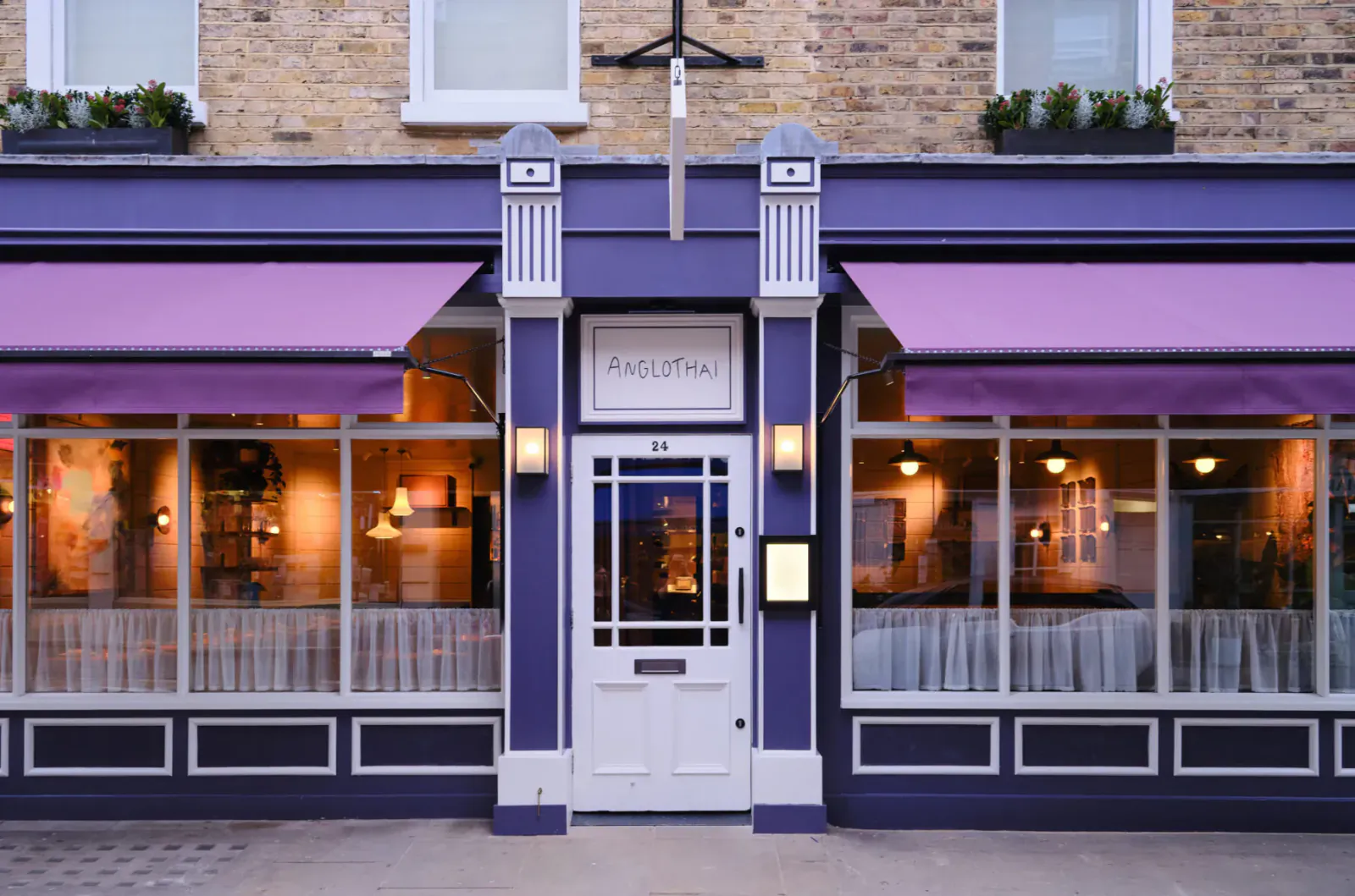 Eels Pie exterior: Georgian brick building with purple awnings, large windows showing warmly lit dining area, and purple front door.