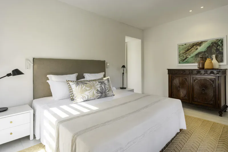 Bright, airy bedroom in Villa Diamond, Mauritius, with white bed, patterned pillows, wood cabinet, and natural light.