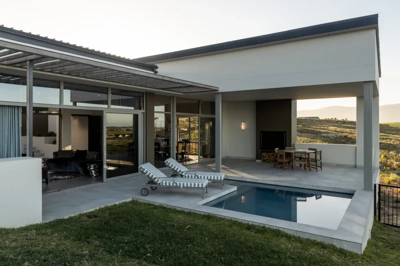 Contemporary house at Benguela Cove wine estate with pool, loungers, patio, and hillside views at sunset.