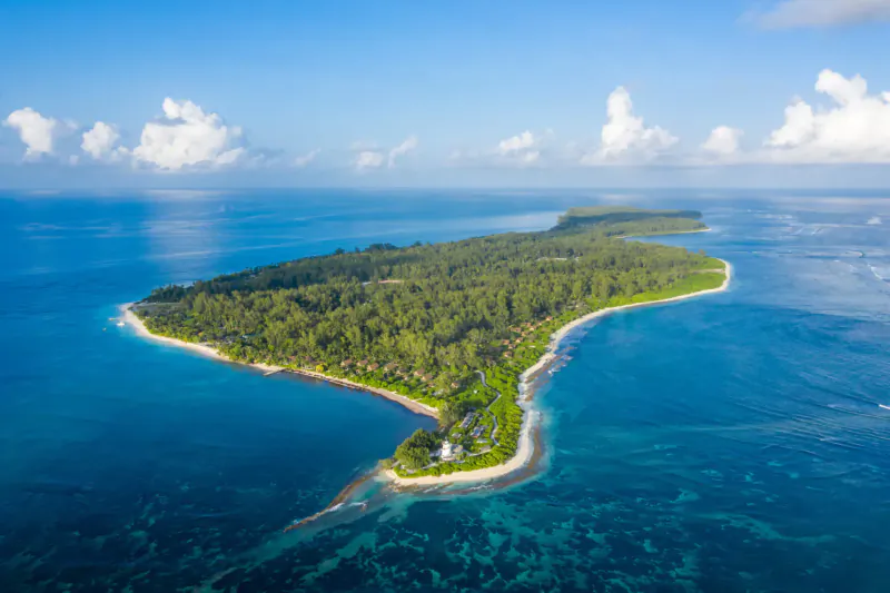 Aerial view of lush green Desroches Island with white beaches, turquoise ocean, and Four Seasons villa.