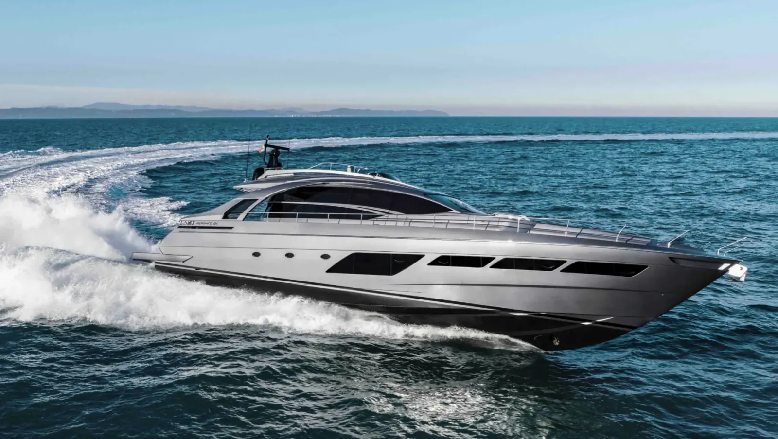 Sleek silver Pershing luxury yacht speeding across the sea, creating white waves, with distant coastline.