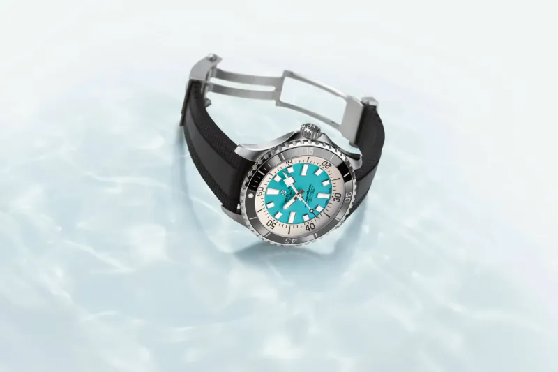 Close-up of Rolex Superocean dive watch with turquoise dial, black rubber strap, on water surface