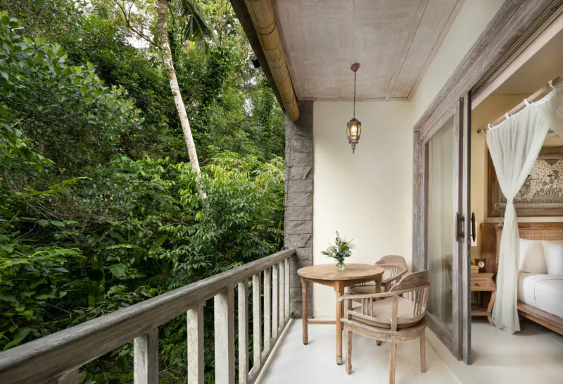 Kayon Resort Bali balcony with wooden table, chairs, flowers overlooking lush tropical jungle and bedroom suite.