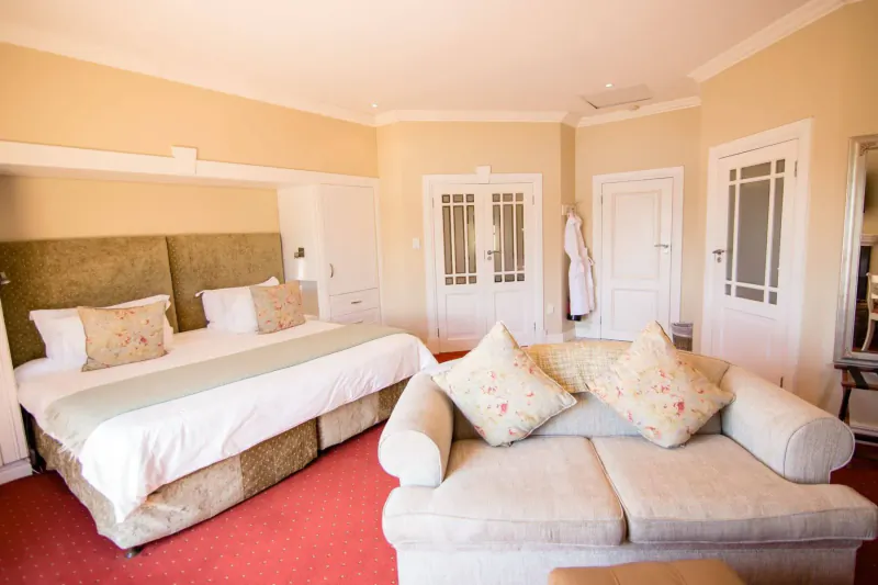 Cozy hotel room at Walkersons Hotel & Spa with king bed, floral pillows, beige sofa, and red carpet.