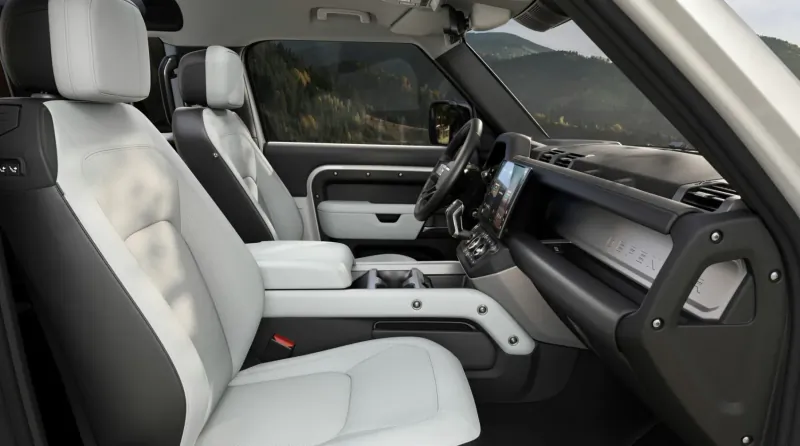 Land Rover Defender interior with light gray leather seats, modern dashboard, and mountain view through windows.