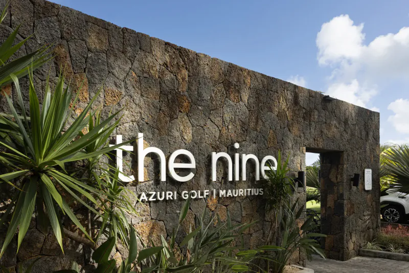 Stone entrance sign 'The Nine' at Azuri Golf Mauritius with palms and open gate