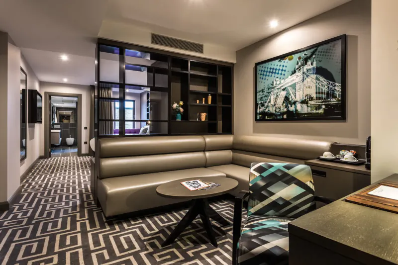 Stylish Courthouse Hotel Shoreditch suite with L-shaped sofa, desk, geometric rug, and cityscape artwork
