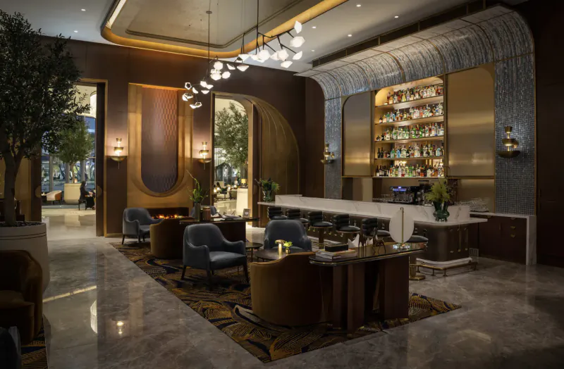 Elegant modern bar lounge at Address Grand Creek Harbour with wooden shelves of liquor bottles, pendant lights, plush chairs, and potted trees.