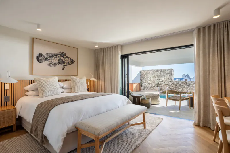 Spacious Oyster Suite bedroom at Abalone Hotel with king bed, fish art, open doors to balcony and ocean view.