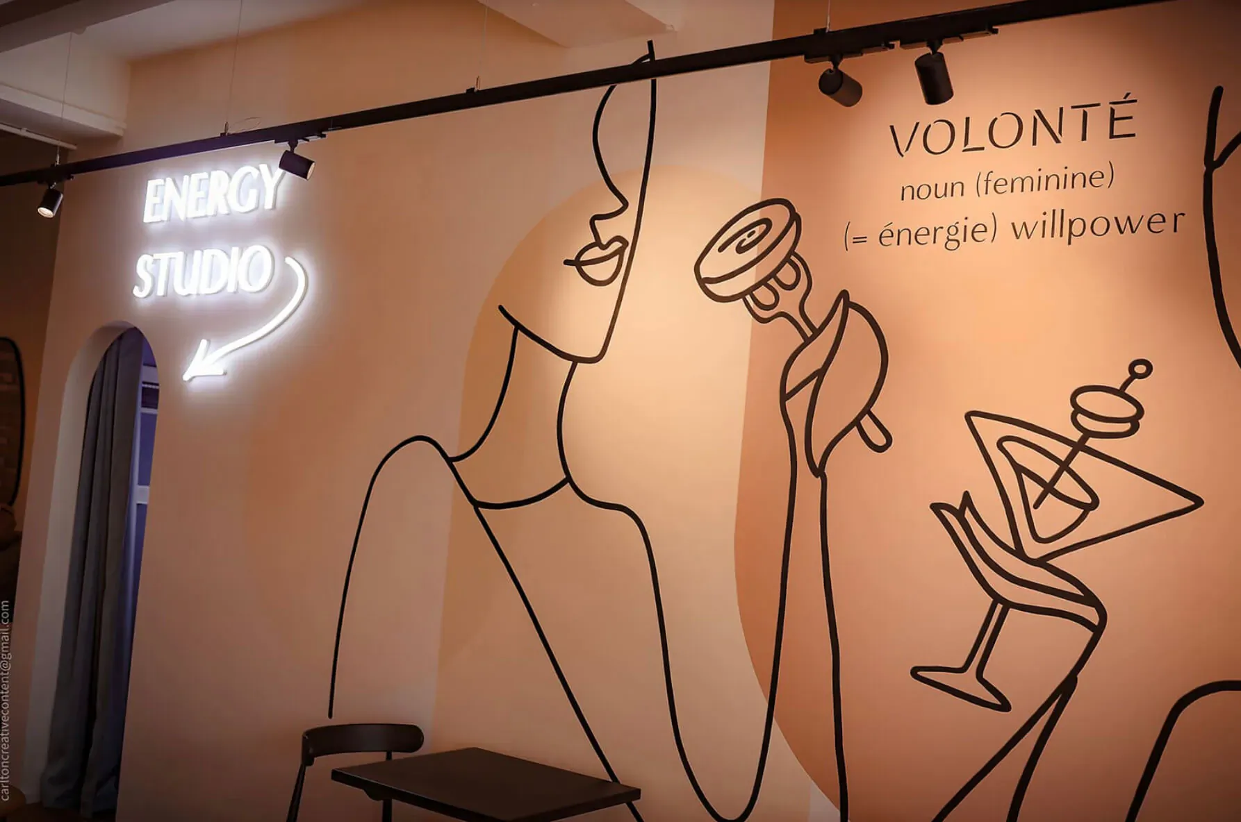 Energy Studio wall mural at Volonté: Stylized woman holding donut and cocktail, neon 'ENERGY STUDIO' sign, '[énergie] willpower' text.