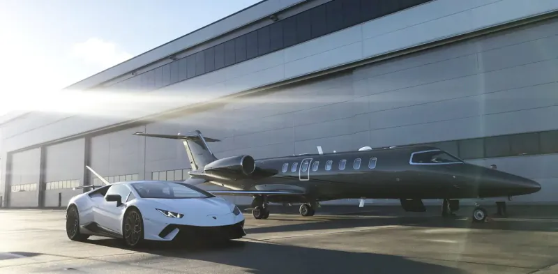 White Lamborghini Huracán parked in front of sleek black private jet at modern hangar, sunny day.