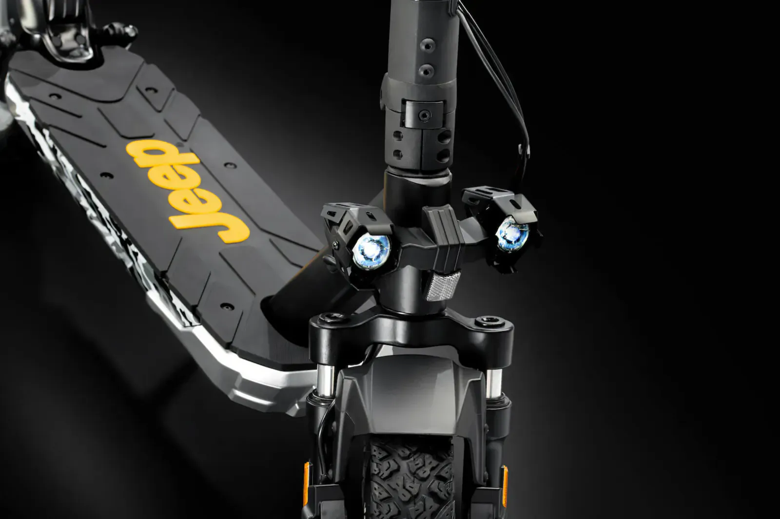 Jeep-branded electric scooter close-up, front view with illuminated headlights and rugged black deck on black background.