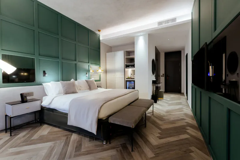 Elegant hotel room at Embassy Valletta with green paneled walls, white king bed, chevron wood floor, and modern furnishings.