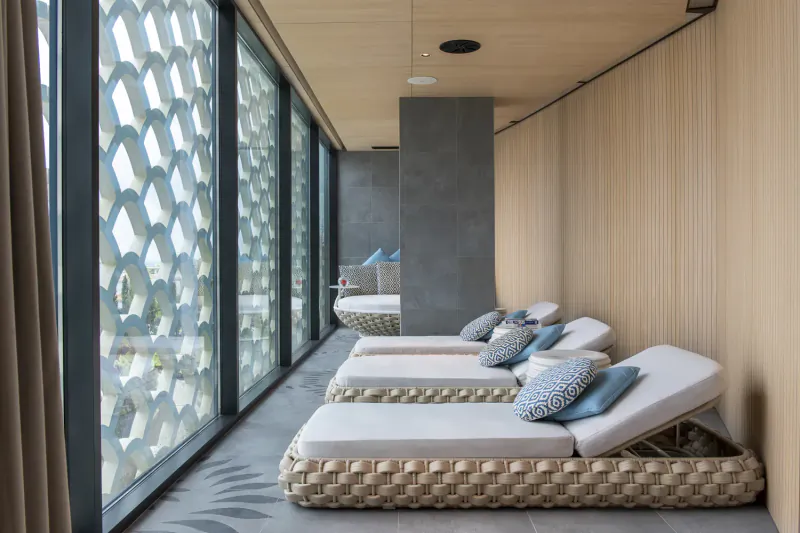 Modern spa lounge at W Algarve Hotel with wicker loungers, blue pillows, and latticed windows.