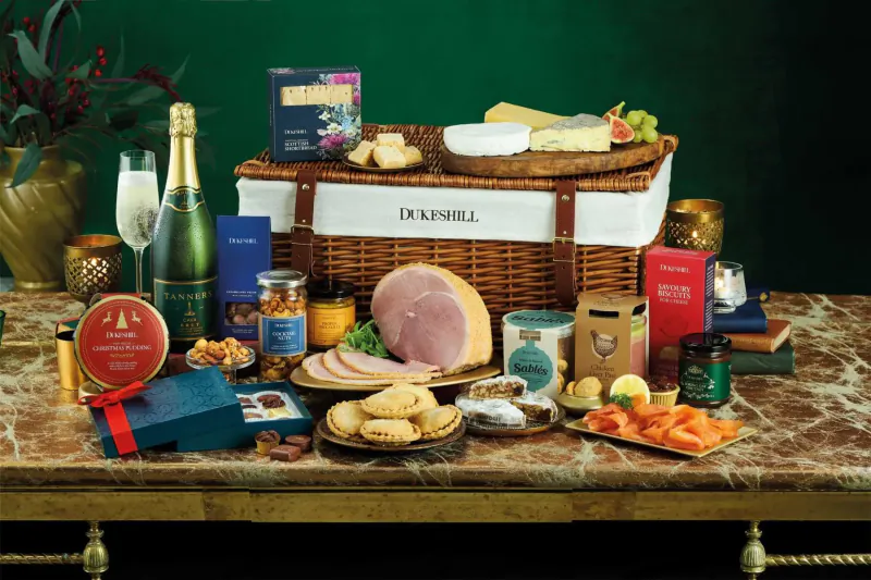 Dukeshill luxury Christmas hamper on marble table with ham, cheese, salmon, cake, champagne, and festive treats.