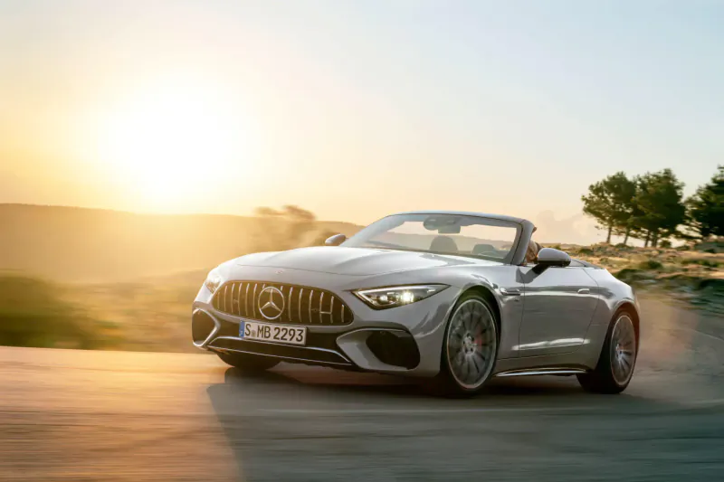 Silver Mercedes-AMG SL convertible speeding on curvy road at sunset with hills and trees