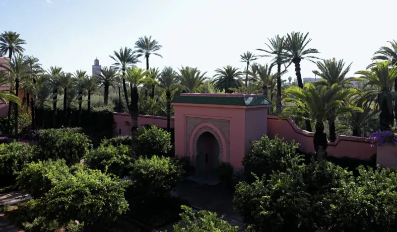Pink Moroccan archway in lush palm and orange tree garden at Royal Mansour Marrakech medina, with distant statue.