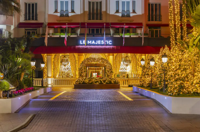 Le Majestic hotel entrance at night, festooned with Christmas trees, lights, garlands, and 'LE MAJESTIC' sign.