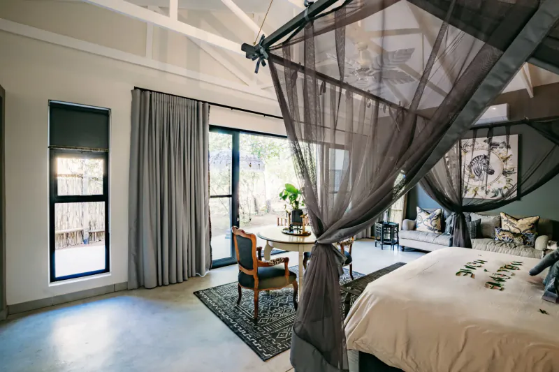Luxurious bedroom in Safari Moon lodge with canopy bed, armchairs, table, and view of bushveld.